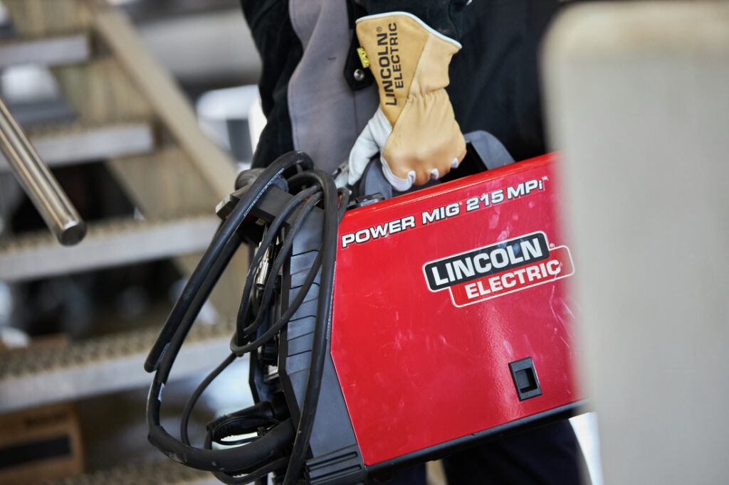 welder carrying a lincoln electric power mig 215 mpi