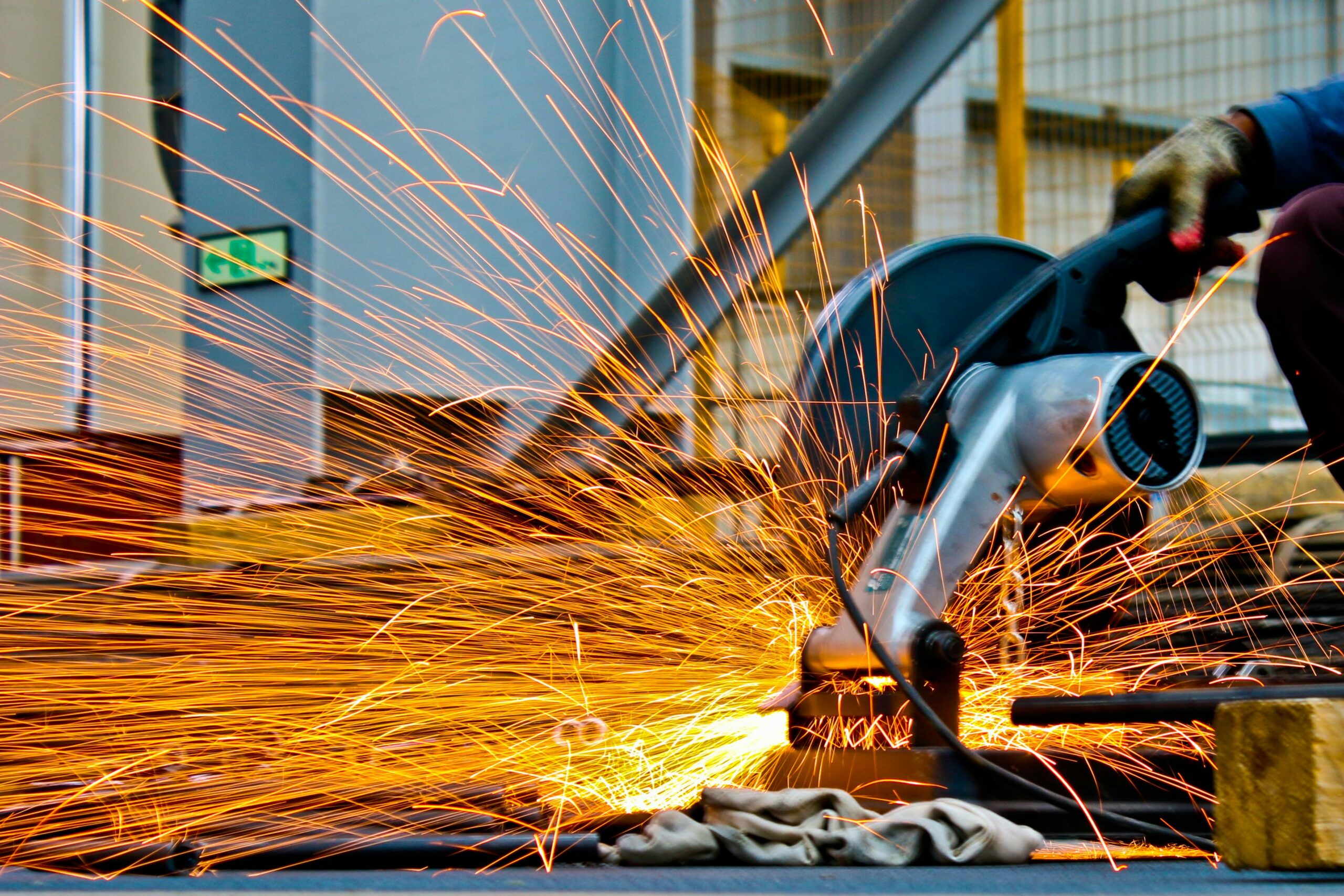 A welder fuses metal outdoors using a welding machine under bright summer sunlight.